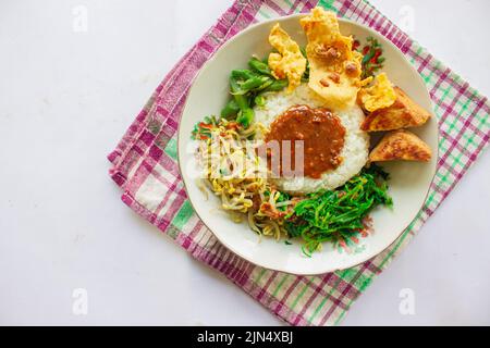 Nasi Pecel oder sego Pecel ist ein traditionelles javanesisches Reisgericht aus gedünstetem Reis mit Gemüsesalat, Erdnusssauce, Tempeh, Tofu-Bohnensprossen und Crackern Stockfoto