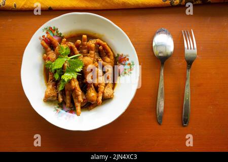 Würzige Hähnchenfüße mit Sellerie, Chili, Zwiebel, Knoblauch, serviert mit einem weißen Teller auf dem Tisch Stockfoto