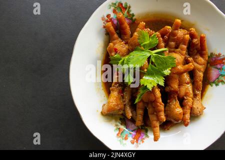 Würzige Hähnchenfüße mit Sellerie, Chili, Zwiebel, Knoblauch, serviert mit einem weißen Teller auf dem Tisch Stockfoto