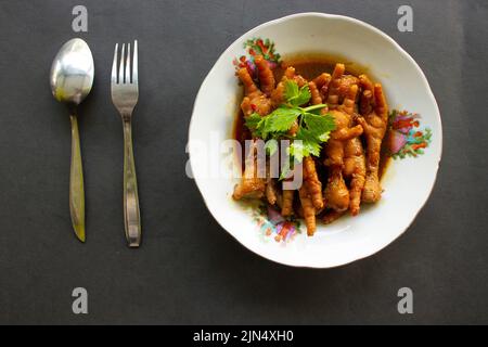 Würzige Hähnchenfüße mit Sellerie, Chili, Zwiebel, Knoblauch, serviert mit einem weißen Teller auf dem Tisch Stockfoto