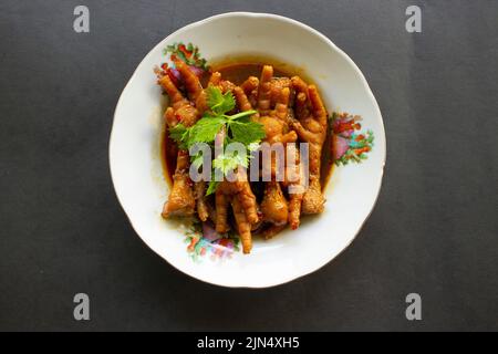Würzige Hähnchenfüße mit Sellerie, Chili, Zwiebel, Knoblauch, serviert mit einem weißen Teller auf dem Tisch Stockfoto