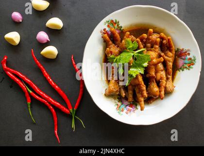 Würzige Hähnchenfüße mit Sellerie, Chili, Zwiebel, Knoblauch, serviert mit einem weißen Teller auf dem Tisch Stockfoto