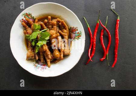 Würzige Hähnchenfüße mit Sellerie, Chili, Zwiebel, Knoblauch, serviert mit einem weißen Teller auf dem Tisch Stockfoto
