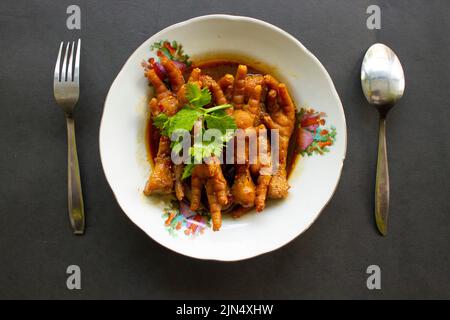 Würzige Hähnchenfüße mit Sellerie, Chili, Zwiebel, Knoblauch, serviert mit einem weißen Teller auf dem Tisch Stockfoto