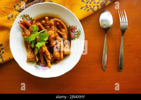 Würzige Hähnchenfüße mit Sellerie, Chili, Zwiebel, Knoblauch, serviert mit einem weißen Teller auf dem Tisch Stockfoto