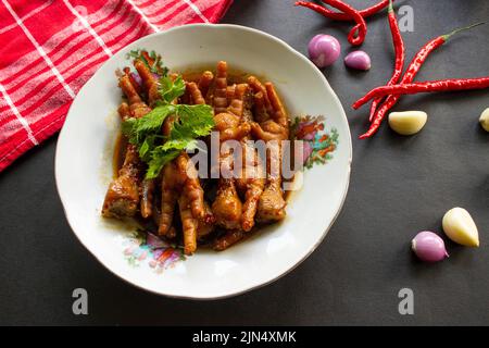 Würzige Hähnchenfüße mit Sellerie, Chili, Zwiebel, Knoblauch, serviert mit einem weißen Teller auf dem Tisch Stockfoto