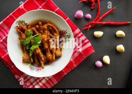 Würzige Hähnchenfüße mit Sellerie, Chili, Zwiebel, Knoblauch, serviert mit einem weißen Teller auf dem Tisch Stockfoto