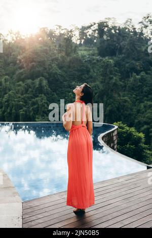 Rückansicht eines jungen weiblichen Models, das am Rand des Pools stand und wegschaute. Kaukasische Frau genießt ihren Urlaub im Luxusresort. Stockfoto