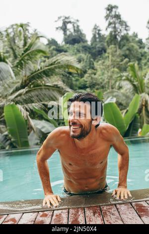 Porträt eines lächelnden jungen Mannes, der aus dem Schwimmbad kommt. Ein hübscher Mann im Pool sieht glücklich aus. Stockfoto