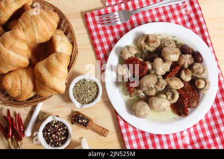 Pilze, sonnengetrocknete Tomaten, Oliven und Kapern in Olivenöl auf rustikalem Holztisch Stockfoto