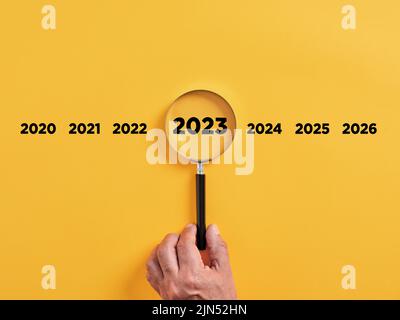 Die männliche Hand hält eine Lupe, die sich auf das Jahr 2023 konzentriert. Fokus auf neue Geschäftsziele, Plan und Strategie des Jahreskonzepts 2023. Stockfoto