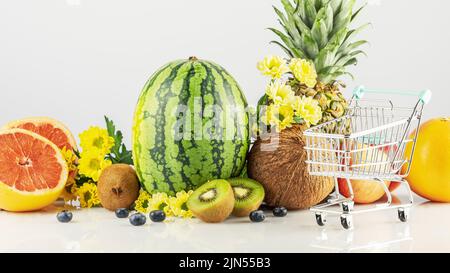 Auswahl an exotischen Früchten. Verkauf Obst Konzept. Natürliche frische Früchte mit Blumen auf weißem Hintergrund mit Einkaufskubus. Obstladen Stockfoto