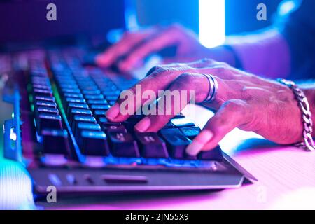 Nahaufnahme der Hände des Spielers mit Neaon-Light-Tastatur für das Spielen von Videospielen - Konzept des Cyberspace, Unterhaltung und Hobbyist. Stockfoto