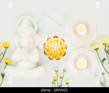 Skulptur von Lord Ganesha mit Blumen und Kerzen auf hellblauem Hintergrund mit Dekorationen. Urlaub in Ganesh Chaturth. Ganesh Festival. Hindu-RE Stockfoto