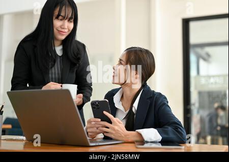 Attraktive junge asiatische Geschäftsfrau, die von ihrer freundlichen Kollegin im Büro einen Arbeitsrat einfordert. Stockfoto