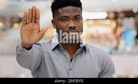 Nahaufnahme eines jungen, seriös selbstbewussten afroamerikanischen Mannes, der die Kamera anschaut, zeigt die Handfläche mit einer Stoppgeste, die den persönlichen Schutz demonstriert Stockfoto