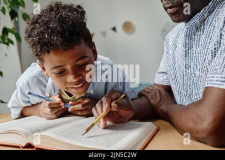 Afrikanischer Junge liest zusammen mit seinem Lehrer am Tisch während der Heimschule Buch Stockfoto