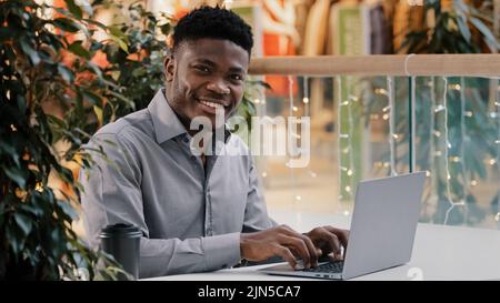 Fokussierter junger männlicher Freiberufler, der online am Laptop tippt, glücklicher Student erfolgreicher Geschäftsmann, der sich mit der Kamera lächelnd umdreht Stockfoto