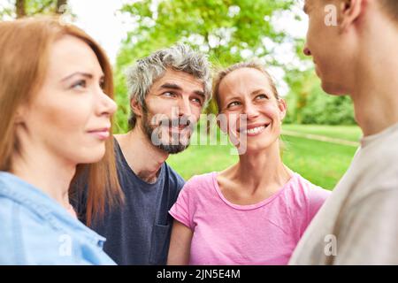 Vier junge Leute als Freunde unterhalten sich in den Sommerferien entspannt im Park Stockfoto