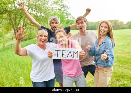 Gruppe junger Menschen, die einen Erfolg feiern und ein Schild mit der Aufschrift Team hochhalten Stockfoto