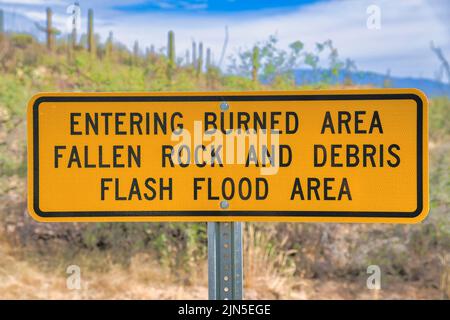 Schilder mit dem Betreten des verbrannten Bereichs Falling Rocks und Debris Flashflood Area in Tucson, AZ. Nahaufnahme eines gelben Schilds gegen das verschwommene Bild Stockfoto