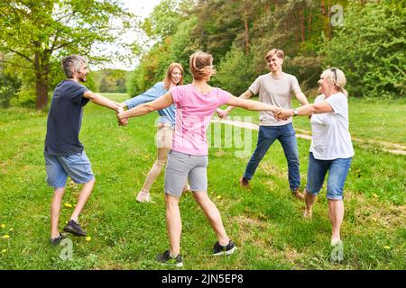 Junge Menschen stehen im Kreis und halten sich bei der Teambuilding-Werkstatt im Park die Hände Stockfoto