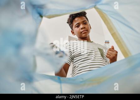 Low-Angle-Ansicht des afrikanischen Jungen, der Plastikflaschen in den Abfalleimer wirft Stockfoto