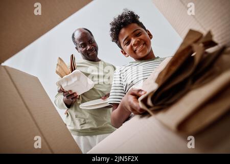 Aus der niedrigen Perspektive sehen Sie, wie Papa seinem Sohn beibringt, den Müll zu trennen, und werfen Papier in einen separaten Kasten Stockfoto