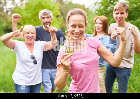 Junge Frau mit Siegermedaille jubelt stolz mit geballten Fäusten und Team im Hintergrund Stockfoto