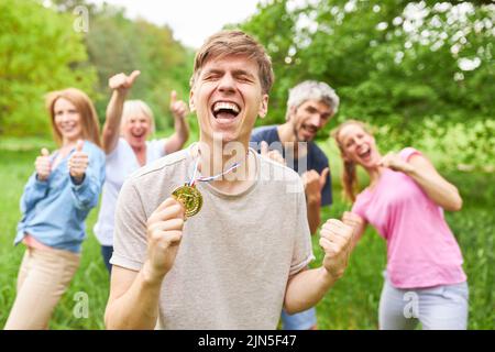 Erfolgreicher junger Mann mit Medaille und Teamjubel nach dem Sieg Stockfoto