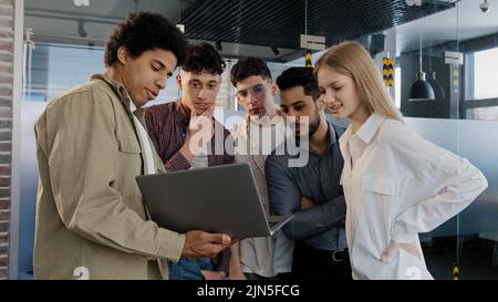 Junge Unternehmensangestellte erklärt Entwicklungsstrategie erzählt neue Ideen und zeigt Arbeitsplan auf dem Laptop dem lächelnden kreativen Team der Kollegen Stockfoto