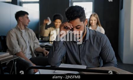 Frustriert unterdrückten indischen Studenten sitzen in der Klasse einsamen jungen Kerl leidet unter Missbrauch Mobbing von Klassenkameraden Spott schlechte Haltung verärgert Stockfoto