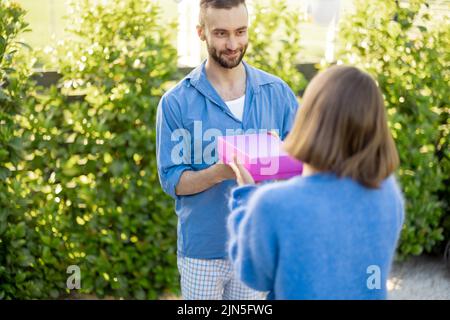 Der Mann schenkt seiner Frau ein Geschenk in einer rosa Schachtel und feiert im Freien Stockfoto