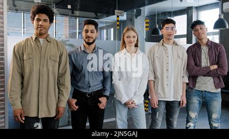 Junge, glückliche Mitarbeiter stehen in Reihe und blicken auf die Kamera, lächeln verschiedene Kollegen und posieren im Büro fünf selbstbewusste, professionelle Geschäftsleute Stockfoto