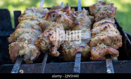 Zubereitung von gegrilltem Schweinekebab. Nahaufnahme der Draufsicht des Grillens von frischem Fleisch auf Metallspießen Stockfoto