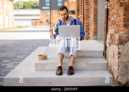 Stilvoller Kerl arbeitet auf einem Laptop-Computer auf einer Straße Stockfoto