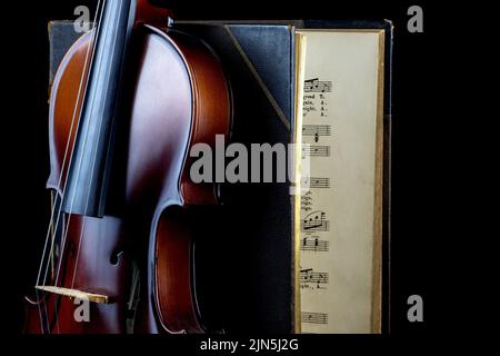 Aufrechte Geige vor einem alten Musikbuch auf schwarzem Hintergrund Stockfoto