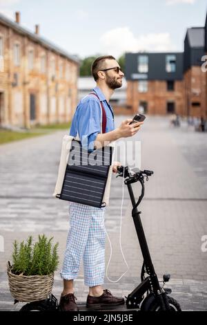 Stilvoller Kerl fährt Elektroroller und nutzt Handy unterwegs Stockfoto