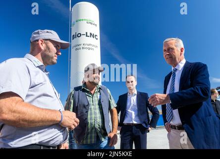 Darchau, Deutschland. 09. August 2022. Der ehemalige Bundespräsident Christian Wulff (r) spricht mit den Landwirten vor der nach Angaben des Herstellers ersten kompakten Bio-LNG-Anlage auf dem Gelände der Agrarvereinigung Darchau. In Zukunft wird die Anlage in der Lage sein, im Inland produzierten grünen Kraftstoff für den schweren Lkw- und Busverkehr zu liefern. Die Anlage soll jährlich etwa 1,3 Millionen Liter fossilen Diesel ersetzen und bis zu 7.000 Tonnen CO2 einsparen. Quelle: Jens Büttner/dpa/Alamy Live News Stockfoto