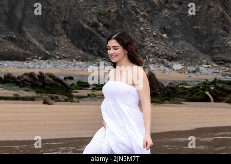 Junge Frau in weißem Kleid, die am Strand spazieren geht Stockfoto