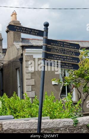 Vertikale Aufnahme eines Vintage-Schildes mit Anweisungen, die auf lokale Touristenattraktionen in Dalkey Stadt zeigen. Zweisprachiger Text in irischer und englischer Sprache. Stockfoto