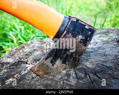 Aufteilen der Maul-Axt im Stumpf. Klein, gebraucht, mit orangefarbenem Kunststoffgriff. Stock Foto. Stockfoto