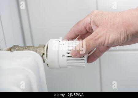 Hand passt den Thermostat auf dem Heizgerät, die Energiekrise mit steigenden Preisen Kräfte, um die Wärme zu reduzieren, Kopierraum, ausgewählten Fokus, enge Tiefe von Stockfoto