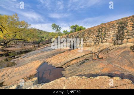 Steinmauer und große Felsen mit Wasserpfütze zwischen den Rissen in Tucson, Arizona. Es gibt eine Form von schrägen großen Felsen mit Wasserpfützen Stockfoto