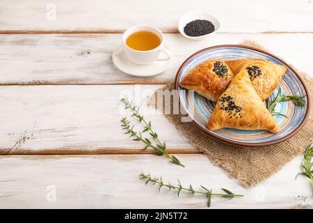 Hausgemachte asiatische Gebäck samosa, Tasse grünen Tee auf weißem Holzhintergrund und Leinentextilien. Seitenansicht, Kopierraum. Stockfoto