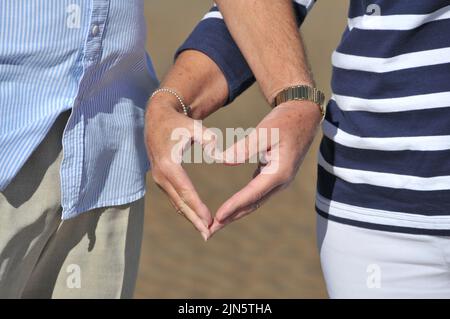Die Kreuze Arme des älteren Paares, die mit den Fingern Herzform bilden Stockfoto