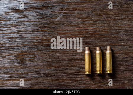 Eine Nahaufnahme von drei leeren Geschossgehäusen auf einem dunklen Holztisch Stockfoto