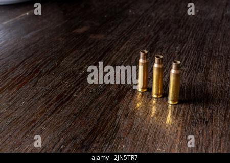 Eine Nahaufnahme von drei leeren Geschossgehäusen auf einem dunklen Holztisch Stockfoto