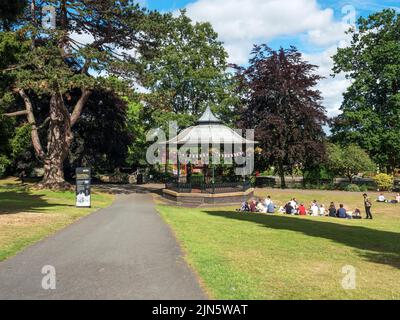 Menschen sitzen auf dem Gras am Bandstand im Priory Park Great Malvern Worcestershire England Stockfoto