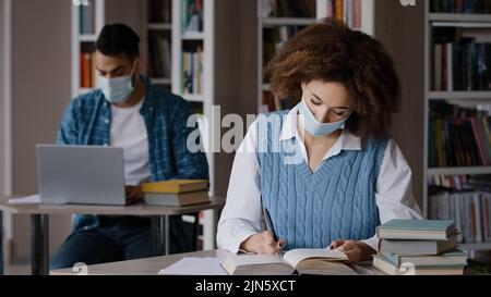 Studenten studieren in der Bibliothek in Schutzmaske erfüllen Quarantäne Maßnahmen junge kluge Mädchen Student Buch lesen auf der Suche nach Informationen in Stockfoto